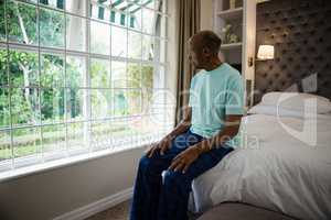 Thoughtful senior man sitting by window in bedroom