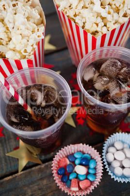 Popcorn, confectionery and drink arranged on wooden table with 4th july theme