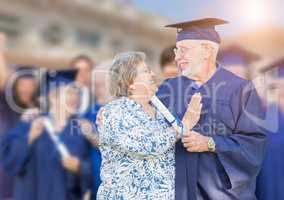 Senior Adult Male In Cap and Gown Being Congratulated By Wife At