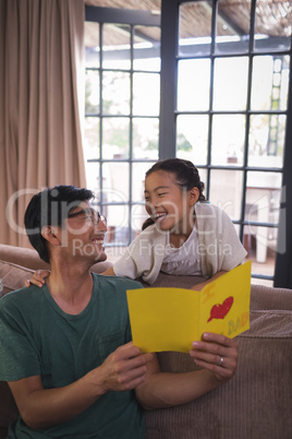 Father and daughter holding greeting card in living room