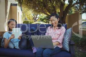 Mother and daughter using digital tablet and laptop while relaxing on couch