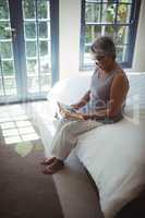 Senior woman reading book while sitting on bed in the bed room