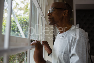 Senior man wearing eyeglasses while looking out through window