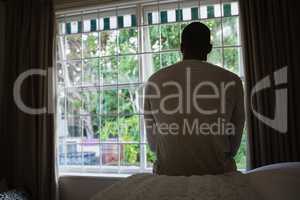 Rear view of man sitting on bed against window