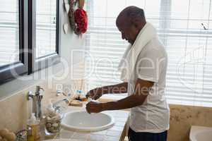 Senior man holding toothpaste and brush by sink in bathroom