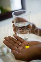 Cropped hands of person holding medicines and drinking water