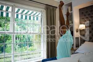 Side view senior man stretching arms while sitting on bed