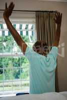 Rear view senior man stretching arms while sitting on bed