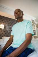 Thoughtful senior man sitting on bed at home