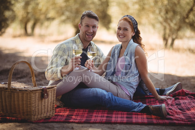 Young couple holding wine glasses while sitting on field at olive farm