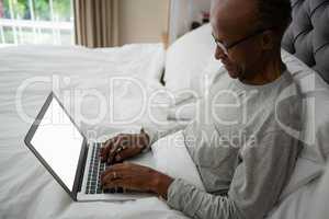 High angle view of senior man using laptop on bed
