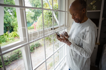Senior man using mobile phone by window at home