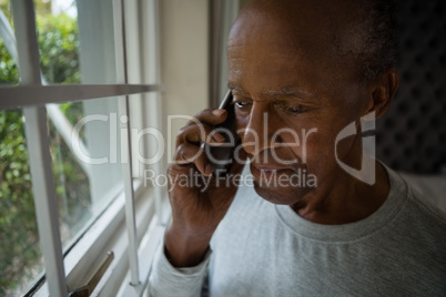 Serious senior man talking on mobile phone by window