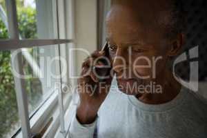 Serious senior man talking on mobile phone by window