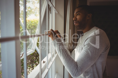 Thoughtful man looking out through window at home