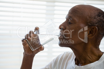 Senior man drinking water against window in bathroom
