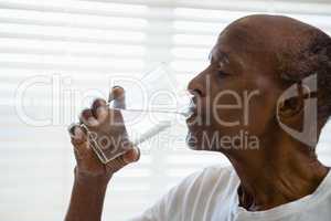 Senior man drinking water against window in bathroom