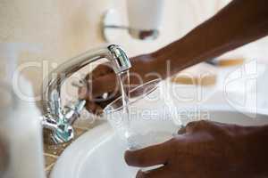 Cropped hands of man filling water in glass at sink