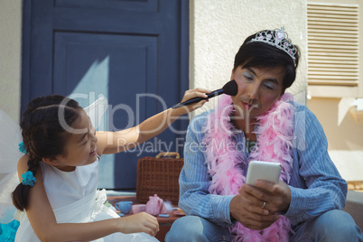 Cute daughter in fairy costume putting makeup on her fathers face