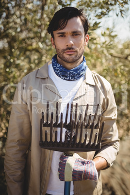 Serious young man with rake standing at olive farm