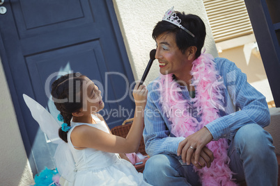 Cute daughter in fairy costume putting makeup on her fathers face
