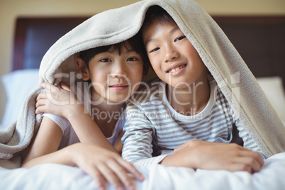 Siblings relaxing under blanket in bedroom