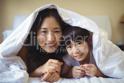Mother and daughter relaxing under blanket in bedroom
