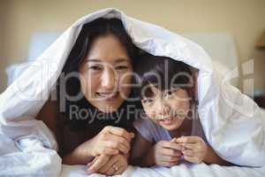 Mother and daughter relaxing under blanket in bedroom