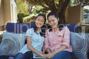 Mother and daughter relaxing on couch outside home