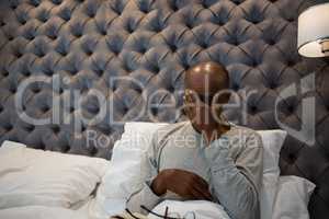 Tired senior man massaging his eyes while sitting on bed