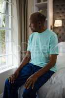 Thoughtful senior man sitting on bed by window