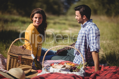 Portrait of young woman sitting with boyfriend on picnic blanket