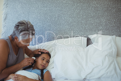 Grandmother checking body temperature of sick granddaughter in bed room