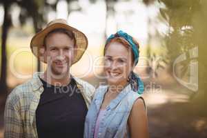 Happy young couple standing by trees at farm