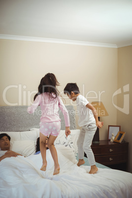 Siblings jumping on bed in bedroom
