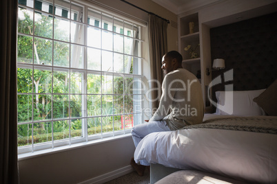 Man sitting on bed by window in bedroom