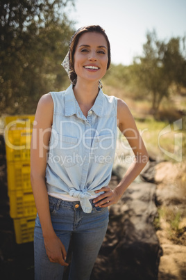 Smiling young woman with hand on hip standing at olive farm