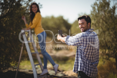 Portrait of man photographing girlfriend at olive farm