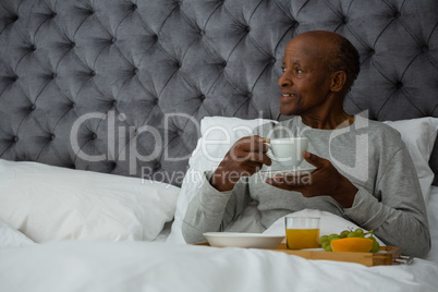 Senior man looking away while having breakfast on bed