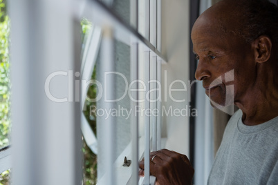 Thoughtful senior man looking out through window