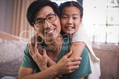 Portrait of smiling father and daughter relaxing on sofa in living room