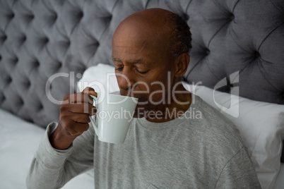 Senior man drinking coffee while sitting on bed