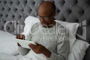 Smiling senior man using digital tablet while resting on bed
