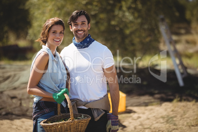 Smiling young couple holding wicker basket at olive farm