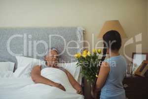 Granddaughter giving flowers to grandmother in bed room