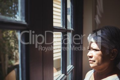 Thoughtful senior woman looking through window in bed room