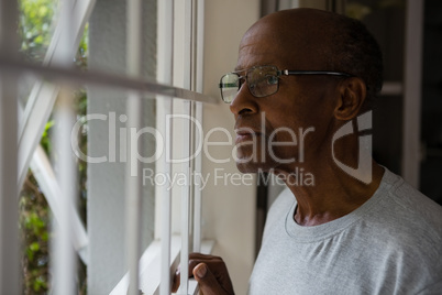 Thoughtful senior man wearing eyeglasses while looking out through window