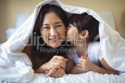 Daughter kissing her mother under blanket in bedroom