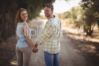 Young couple holding hands while walking on dirt road at olive farm