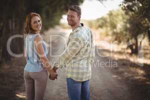 Young couple holding hands while walking on dirt road at olive farm